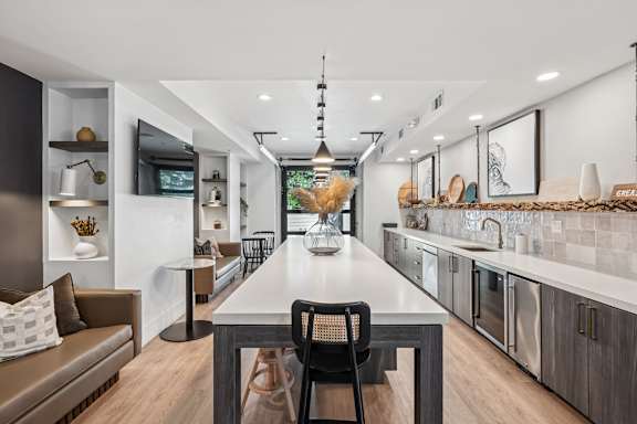 A modern kitchen with a long table and chairs in the middle.
