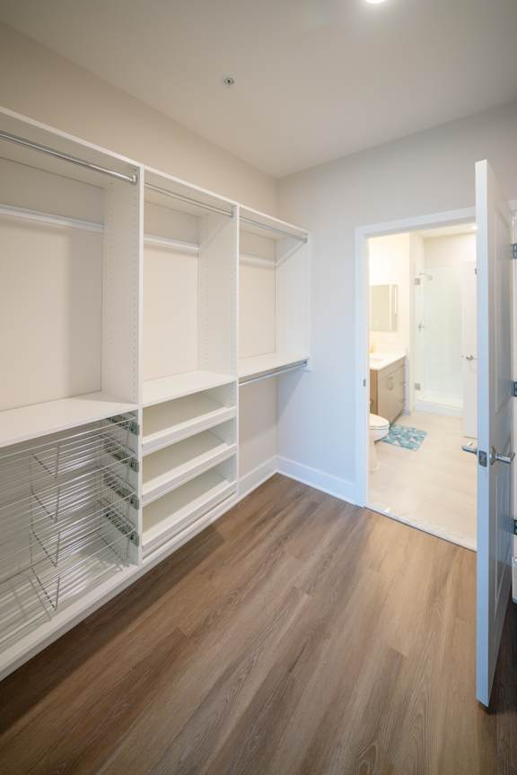 A white closet with shelves and a doorway leading to a bathroom.