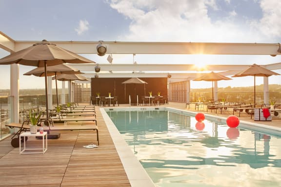 a swimming pool on the roof of a building with tables and umbrellas