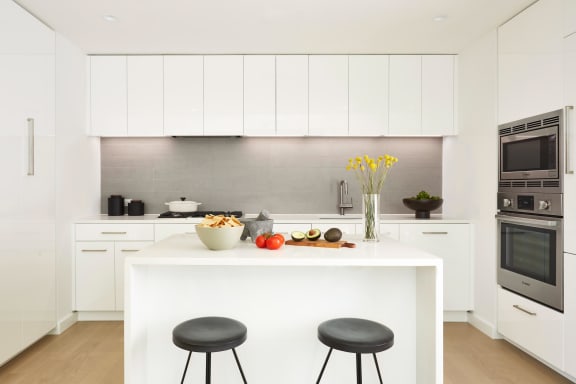 a kitchen with white cabinets and a white island with two black stools