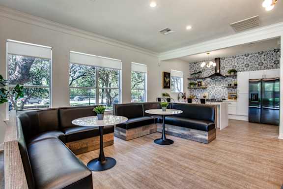A modern clubhouse with black leather furniture and a kitchen in the background.