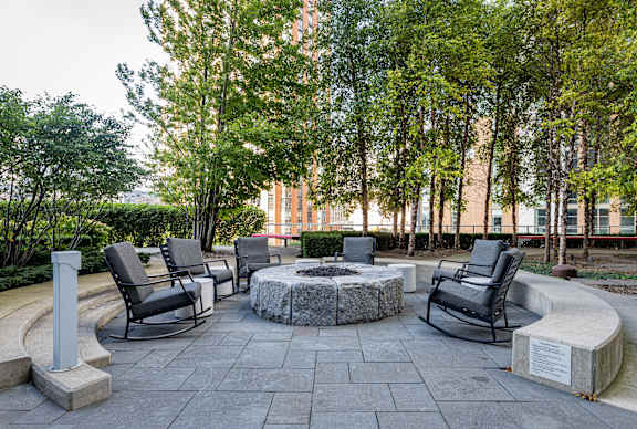 A stone fire pit sits in the middle of a patio surrounded by chairs.