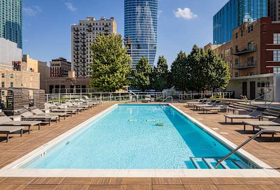 A large swimming pool with a blue tinted water surrounded by a wooden deck and lounge chairs.
