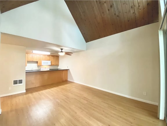 Unfurnished Living room and kitchen areas with wood floors and vaulted dark wooden ceilings at Castlewood Apartments, in Walnut Creek, California