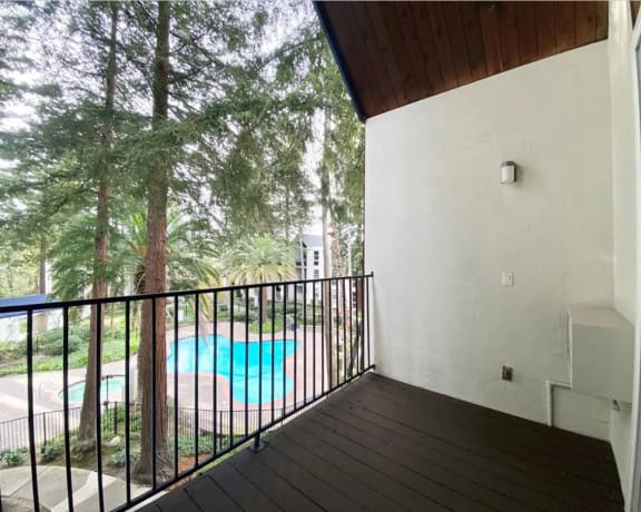 Private balcony with a view of a pool and trees at Castlewood Apartments in Walnut Creek, CA