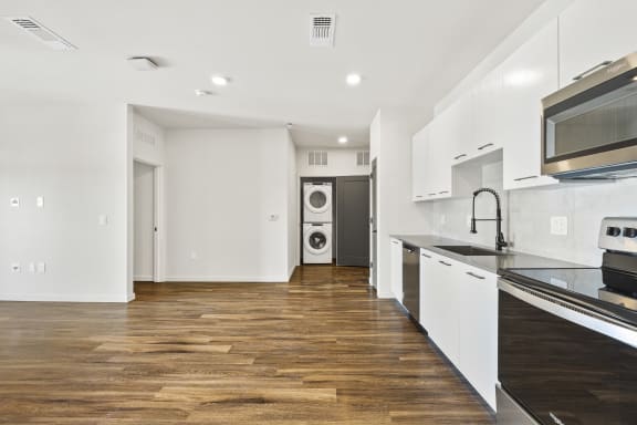 Renovated kitchen with white cabinets, stainless steel appliances, in-unit laundry,  and wood flooring at Azalea Luxury Tampa Apartments