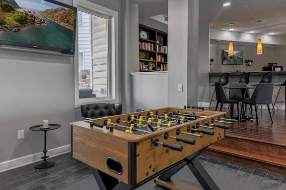 A foosball table is in the middle of a room with a TV and a dining table.