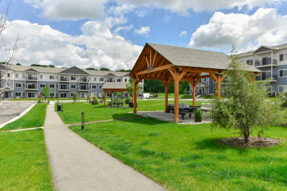 a pathway leading to an open pavilion in a park with apartments in the background at The Lodge at Overland, Rochester, MN, 55901