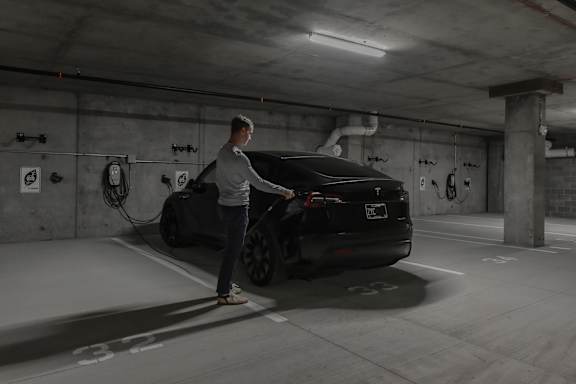 A man is charging an electric car in a parking garage.