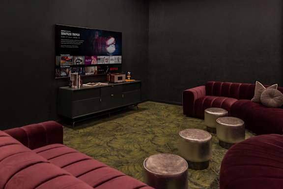 A room with a red couch and ottoman in front of a black wall with a poster on it.