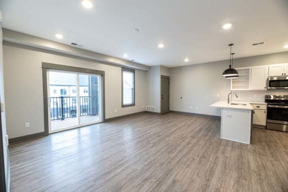 an empty living room with a kitchen and a door at The Commons at Rivertown, Grandville, MI, 49418