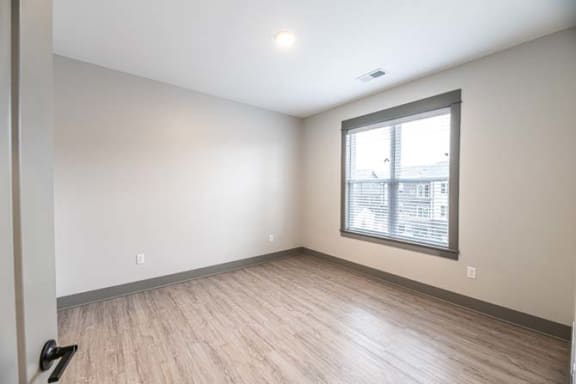 an empty living room with a large window and wooden floors at The Commons at Rivertown, Grandville, 49418