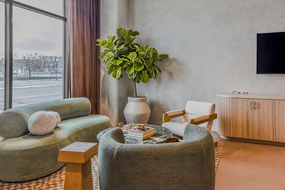 A living room with a green couch, a green armchair, a coffee table, a potted plant, and a TV.