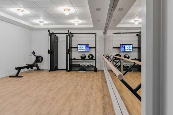 A gym with a wooden floor and a variety of equipment including a squat rack, a bench, and a barbell.