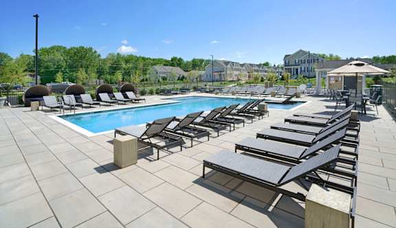A pool with sun loungers and a building in the background at Parc at Princeton Junction Apartments, Princeton, New Jersey