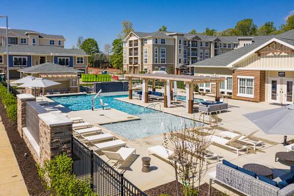 a pool with lounge chairs and umbrellas in front of an apartment building at The Bend Arbordale, Williamsburg, 23188