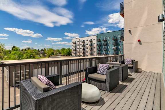 A balcony with black wicker furniture and a blue sky.