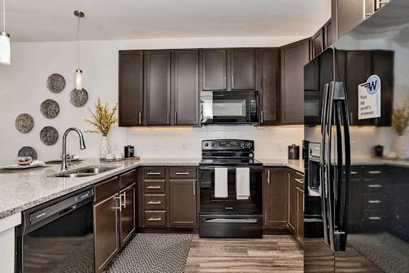 A modern kitchen with dark brown cabinets and black appliances.