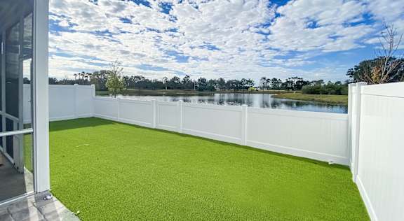 A white fence surrounds a green lawn with a lake and trees in the distance at Artesia at Lakewood Ranch Apartments, Bradenton, 34211