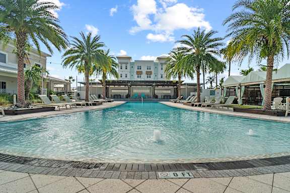 A pool surrounded by palm trees and lounge chairs.