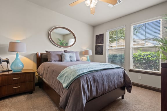 a bedroom with a large bed and two windows at The Millennium Towne Center Apartments, Baton Rouge, LA