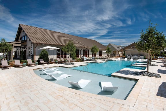 a large swimming pool with lounge chairs and a building at The Cottages at Old Monrovia Apartment , Alabama
