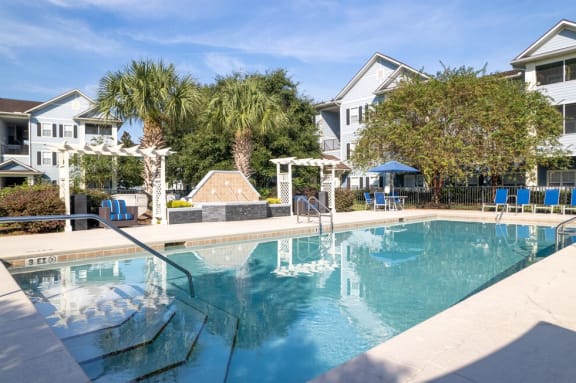 a swimming pool with blue chaise lounge chairs and palm trees in the background at Magnolia Village Apartments, Jacksonville, 32207