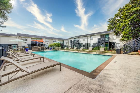 Swimming pool with lounge chairs and umbrellas in front of a building  at Willowick Apartments, College Station, Texas