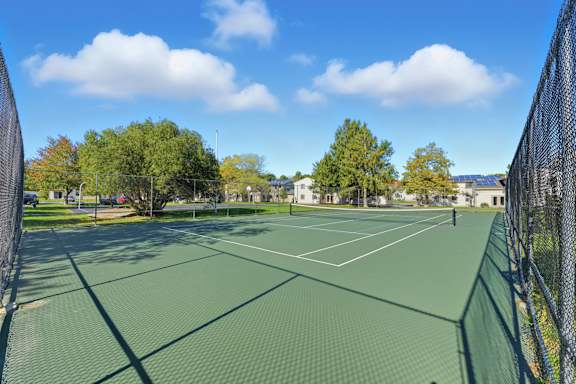 A tennis court surrounded by a fence with trees in the background.