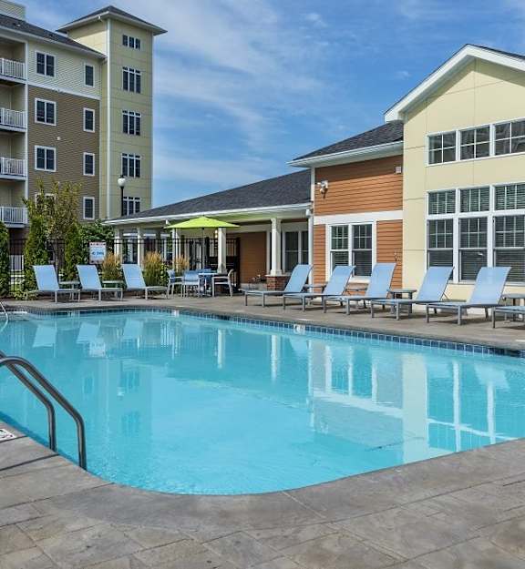 A swimming pool in front of a building with a yellow and brown facade at Axis at Lakeshore Apartments, Bridgewater, Massachusetts