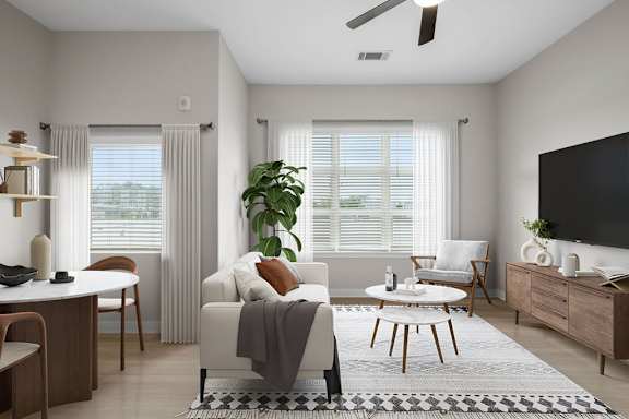 A living room with a white couch, a wooden coffee table, and a large window with white curtains.