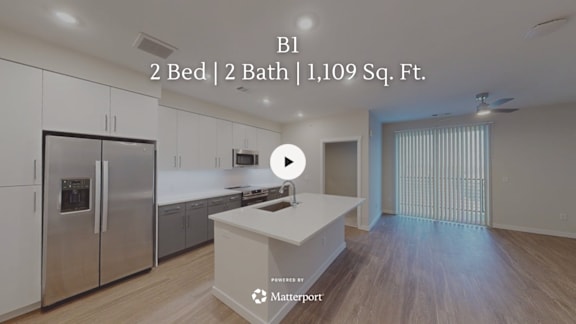 A kitchen with a refrigerator, sink, and a play button overlay.