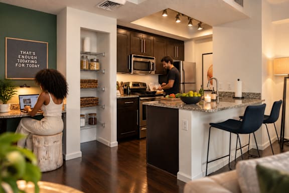 A woman is sitting on a stool at a kitchen island with a man cooking in the background.