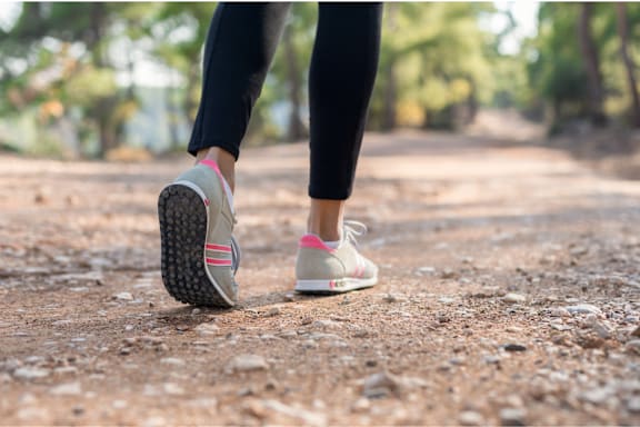 A person is walking on a dirt path with their feet in sneakers.