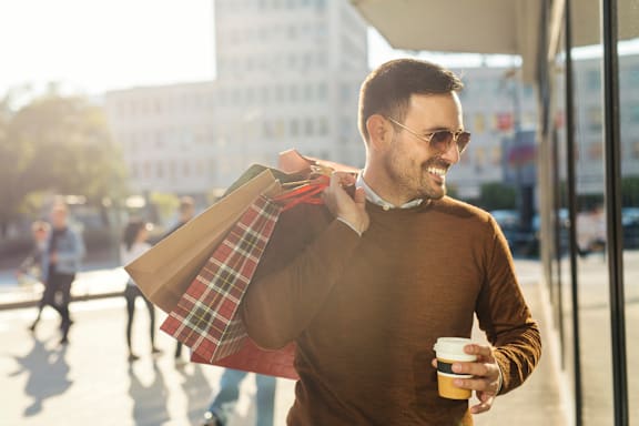 A man is holding a cup of coffee and shopping bags.