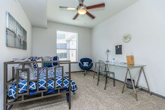 A bedroom with a bed, desk, chair, and a ceiling fan.