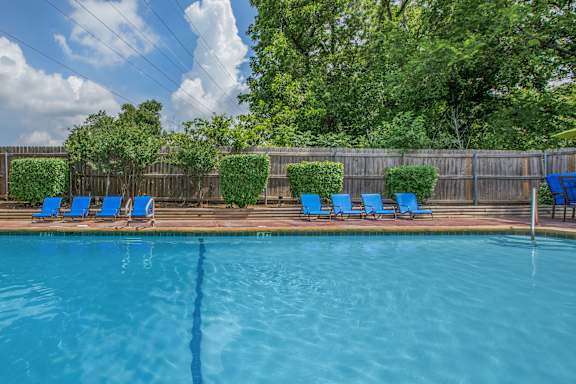 A pool with blue chairs and a fence in the background.