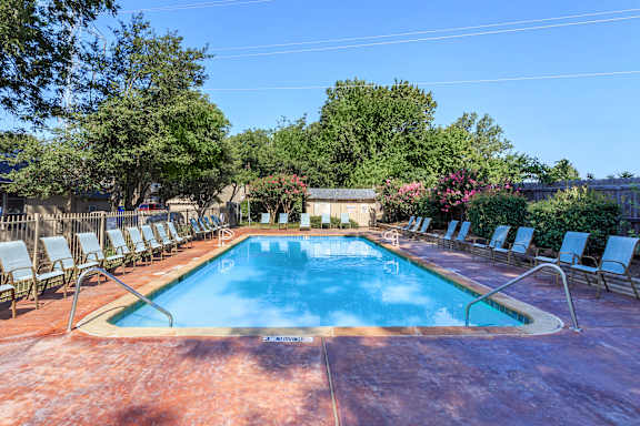 A pool surrounded by chairs and trees.
