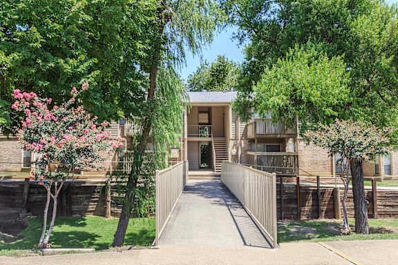 A modern house with a wooden fence and a tree with pink flowers in front.