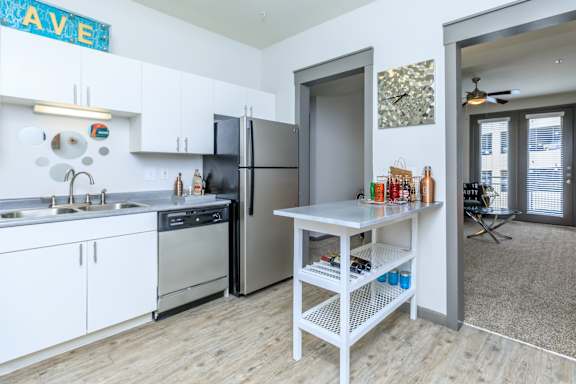 A kitchen with a refrigerator, sink, and a table with bottles on it.