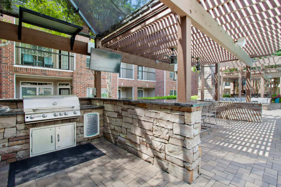 the outdoor kitchen has a grill and a bar with a television