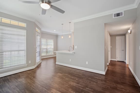 an empty living room with a kitchen and a ceiling fan
