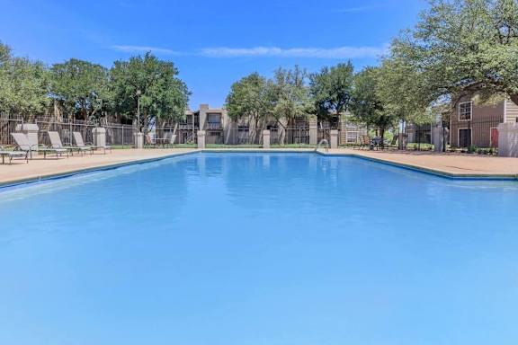 a large swimming pool with trees and apartments in the background