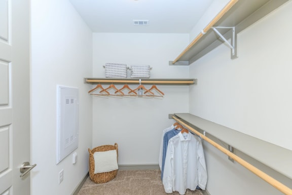 a walk in closet with white walls and shelves and a clothes rack