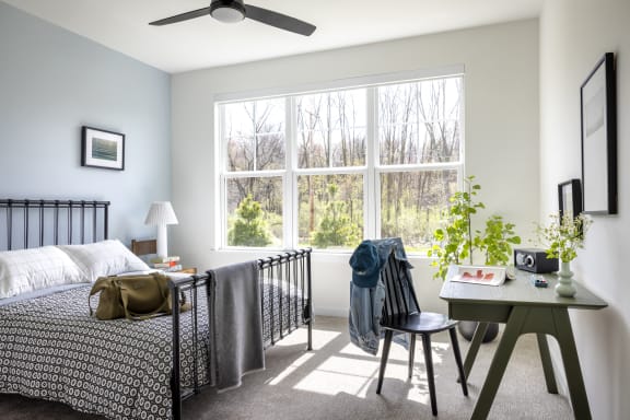 a bedroom with a bed and a large window and a desk with a chair