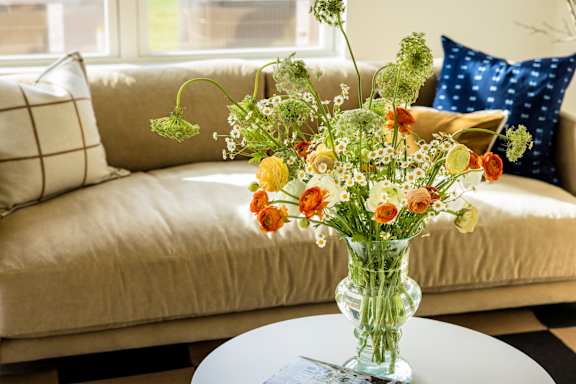 A vase of flowers sits on a table in front of a couch.