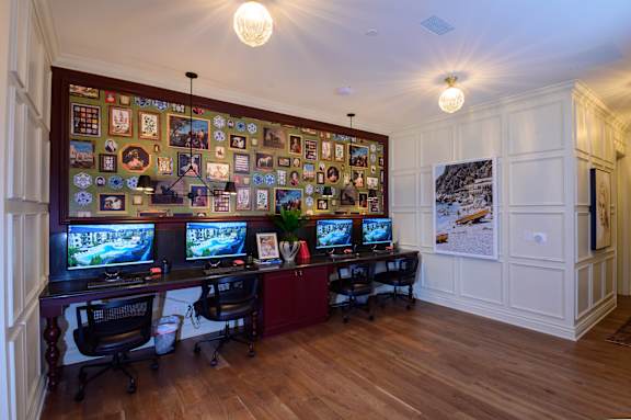 A room with a long wall covered in pictures and two computer monitors.