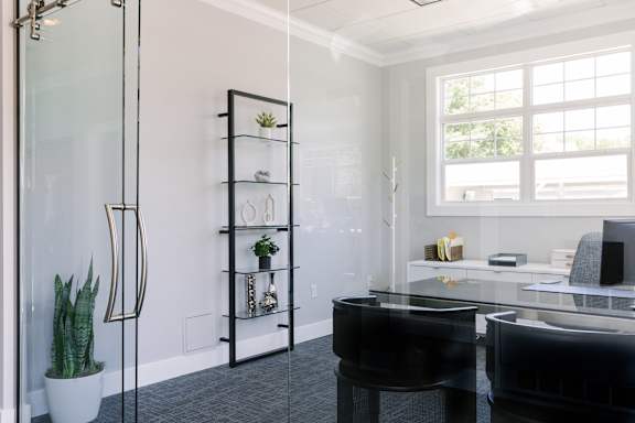 A black piano sits in front of a glass wall in a bright room.