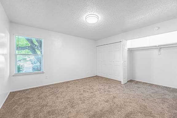 A room with a carpeted floor and a window showing a view of trees and a house.