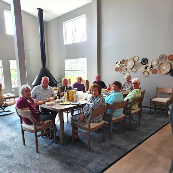 A group of people are sitting around a table in a room with a large fireplace.